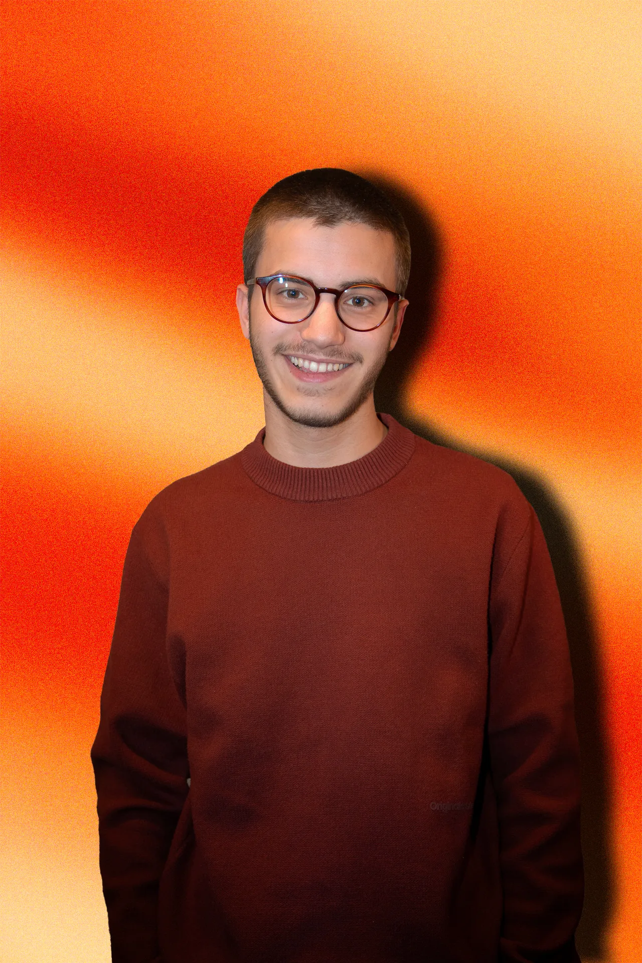 Portrait de Liory Prud’homme, souriant, devant un fond orangé.