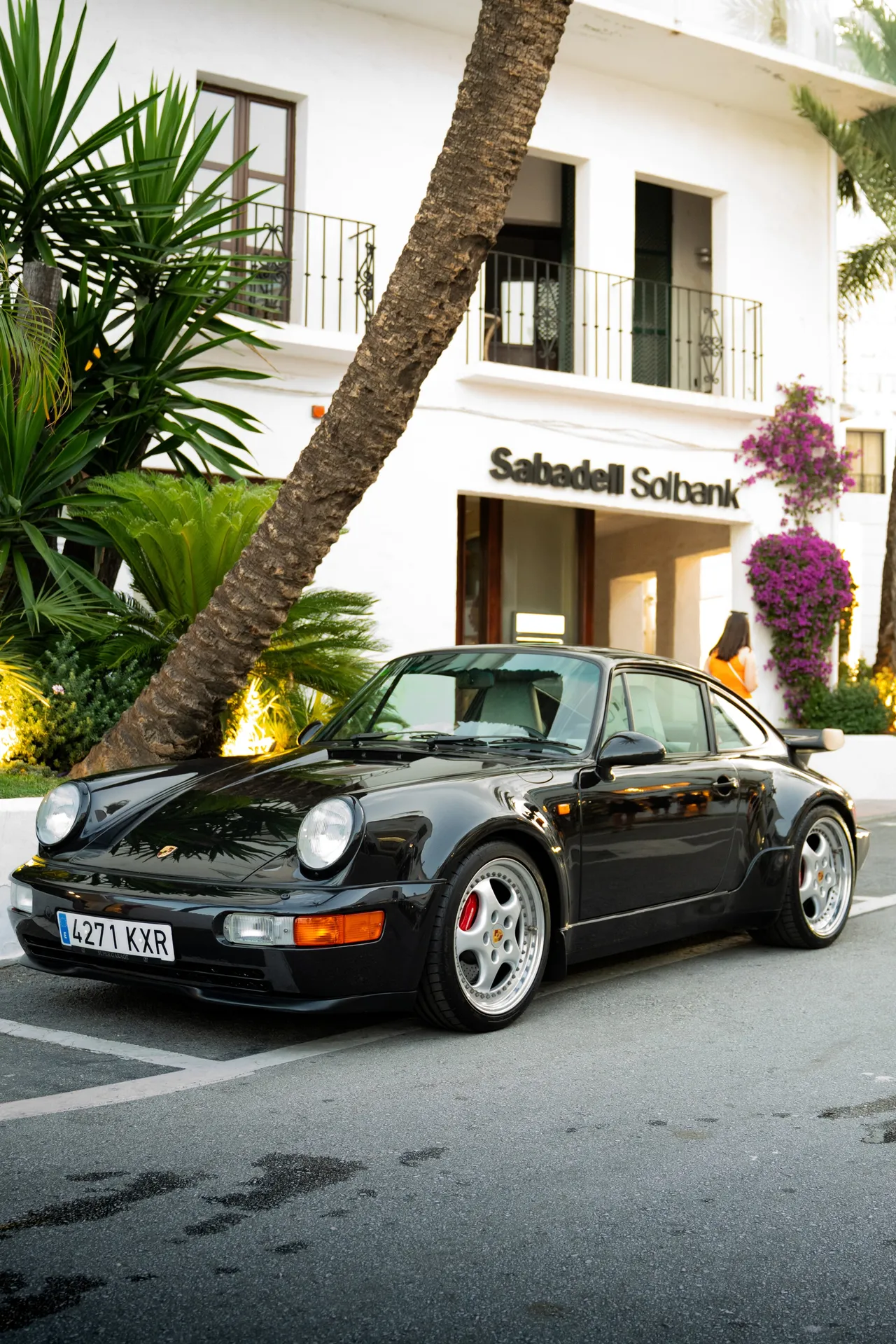 Une Porsche 911 964 Turbo noire garée sous un palmier, devant une façade blanche andalouse.