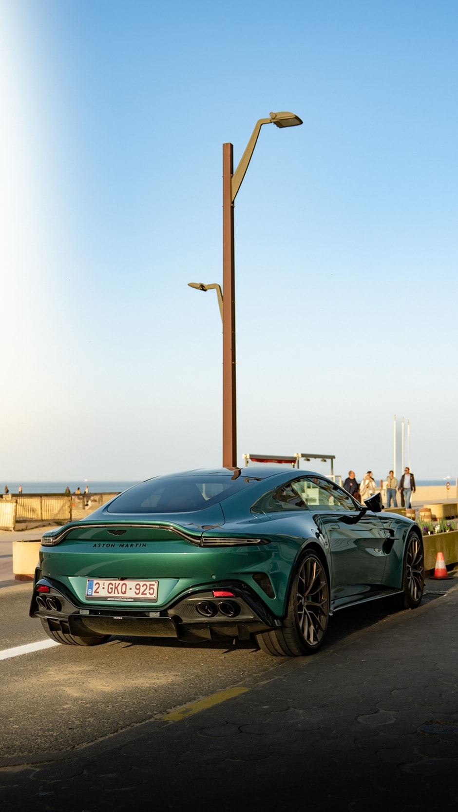 Une Aston Martin Vantage verte garée face à la mer, un lampadaire s’élevant derrière elle.