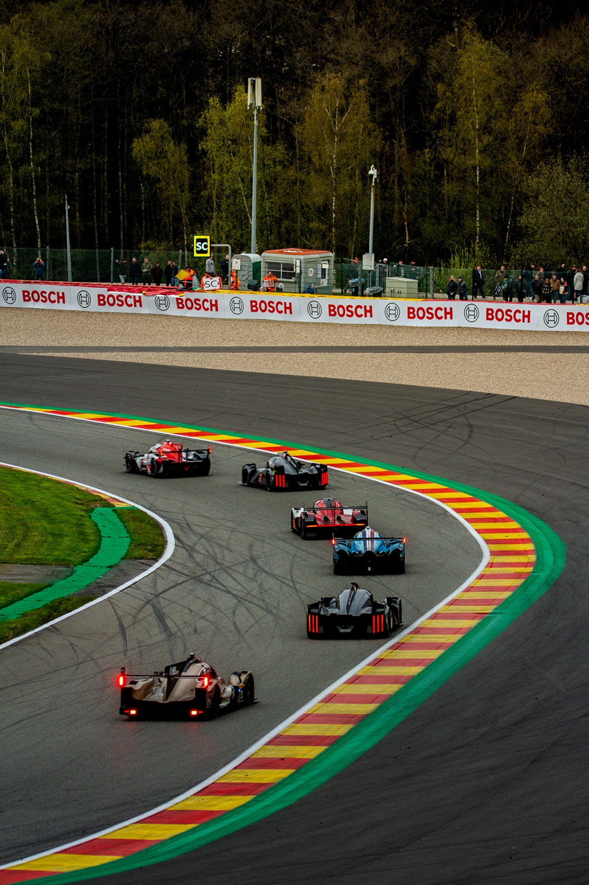 Six prototypes Hypercar et LMP2 en enfilade dans une courbe bordée de vibreurs rouges, jaunes et verts.