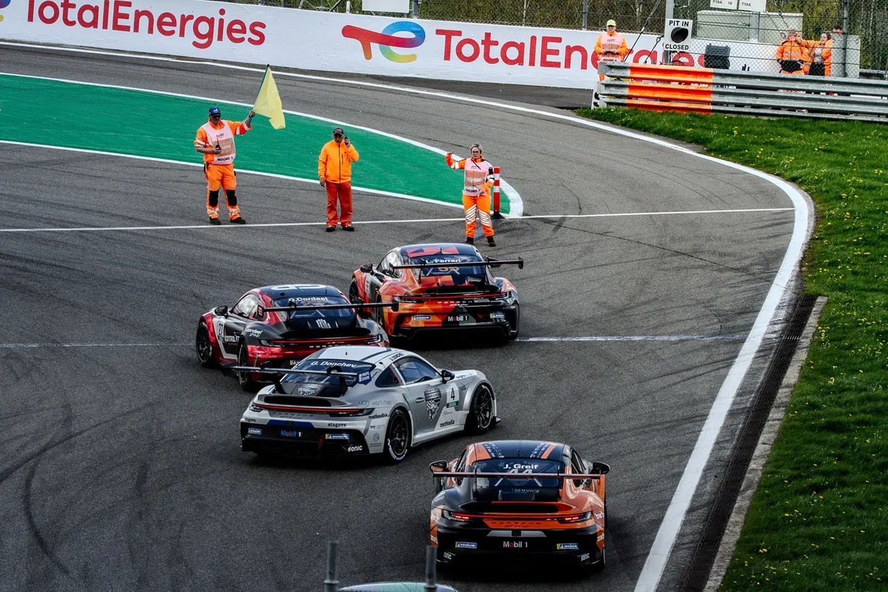Cinq Porsche 911 GT3 Cup en file dans un virage, commissaires agitant le drapeau jaune en bord de piste.