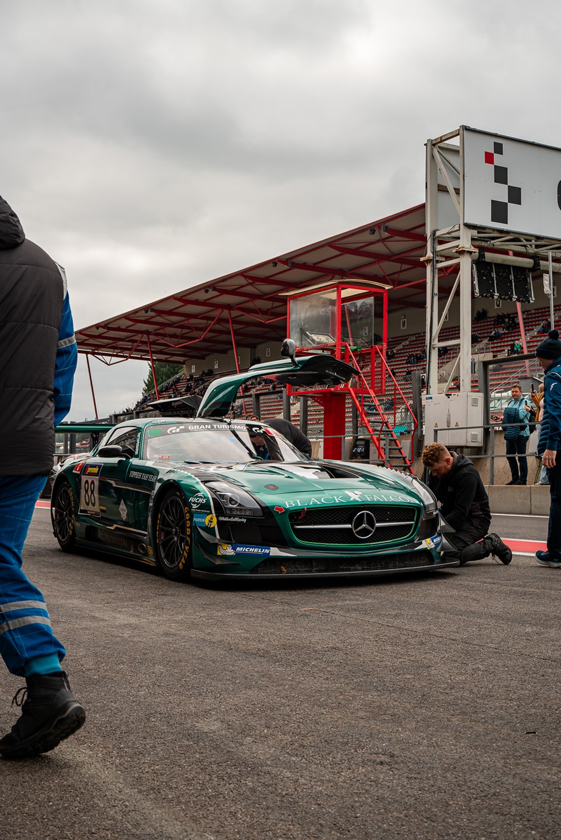 Une Mercedes SLS AMG GT3 verte de l’écurie Black Falcon dans la voie des stands, un mécanicien agenouillé à l’avant.