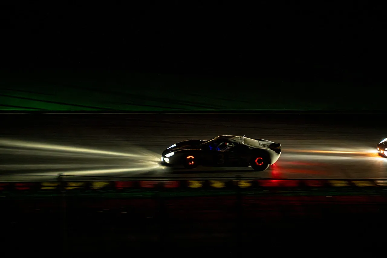 Une Ford GT40 numéro 3 filant dans la nuit, ses phares traçant deux traînées de lumière sur la piste.