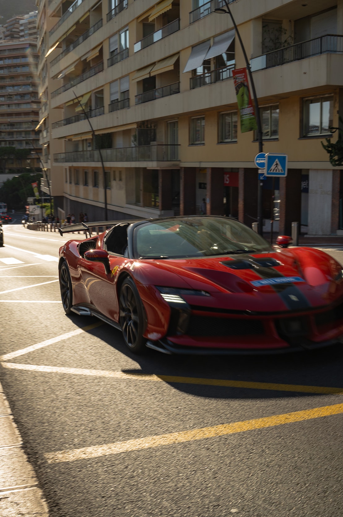 Une Ferrari SF90 rouge remontant une avenue de Monaco dans la lumière rasante du soir.